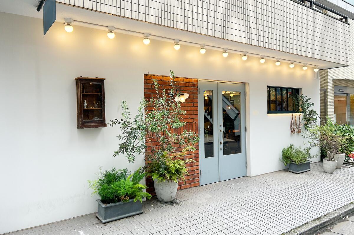 白い壁に水色のドア、植栽のある店舗の外観